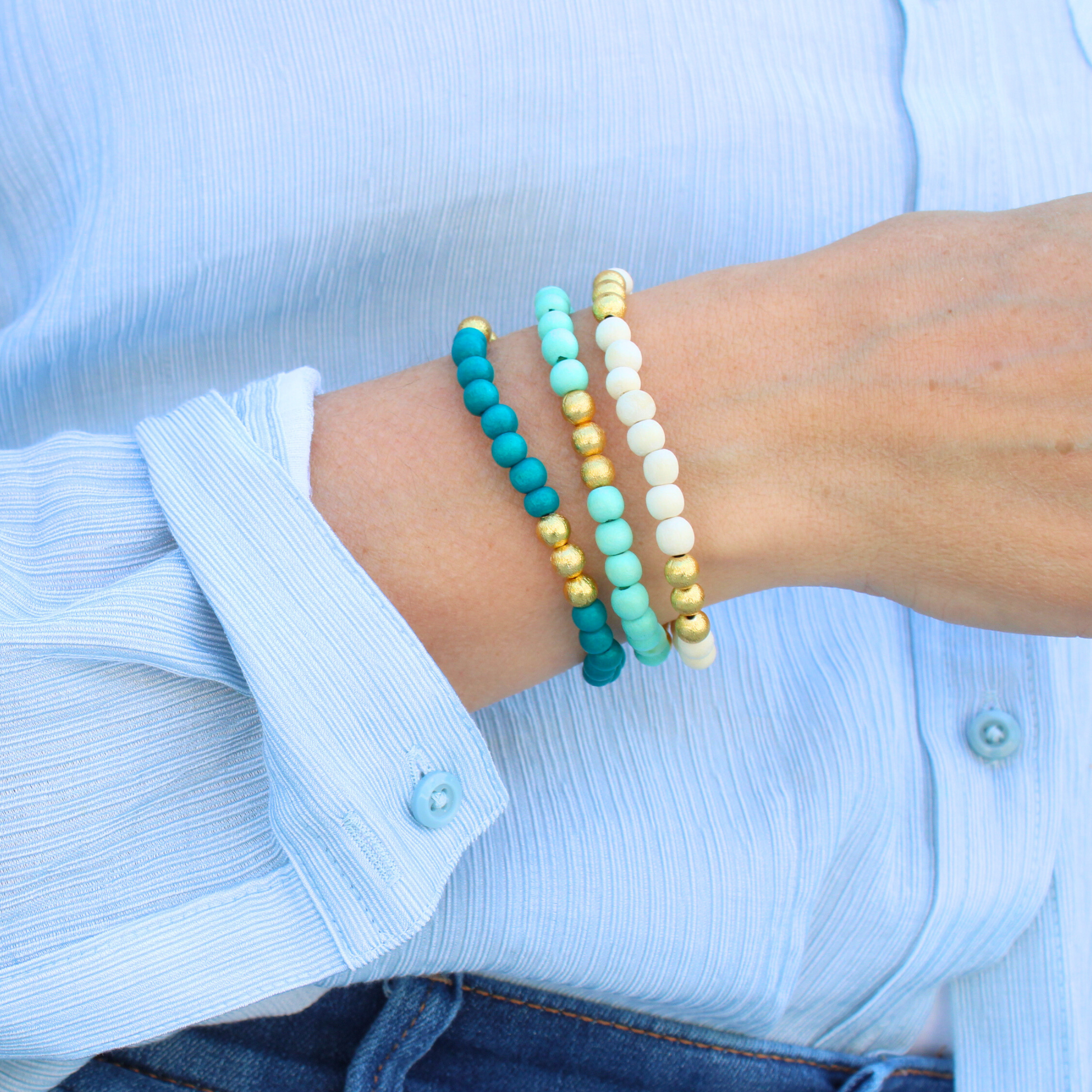 Model wearing 3-peice turquoise, mint and white lightweight wood stretch beaded bracelet set. All three bracelets accented with brushed gold beads.