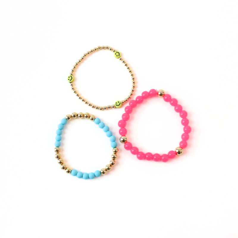 Picture shows a 3-piece bracelet stack flat. This bracelet set has a dainty 18k gold filled beaded bracelet with 3 bright yellow smiley face bracelet. Also designed with blue acrylic beads with 18k gold filled beads. The third bracelet is a pink gemstone beaded bracelet with 3 gold filled round beads.