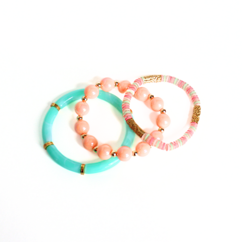 3-Piece chunky beaded bracelet stack. Designed with 12mm round peach iridescent beads and acrylic aqua marble tube bead bangle. A peach and green polymer clay beaded stretch bracelet accented with gold plated flower flats pull this bracelet stack together