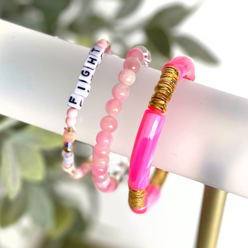 Pink beaded breast cancer awareness bracelet set. This very pink 3-piece bracelet set is curated with pink acrylic bangle, clear round quartz beads, pink beads and word beaded bracelet. Proceeds will be donated to the Susan G. Komen Foundation.