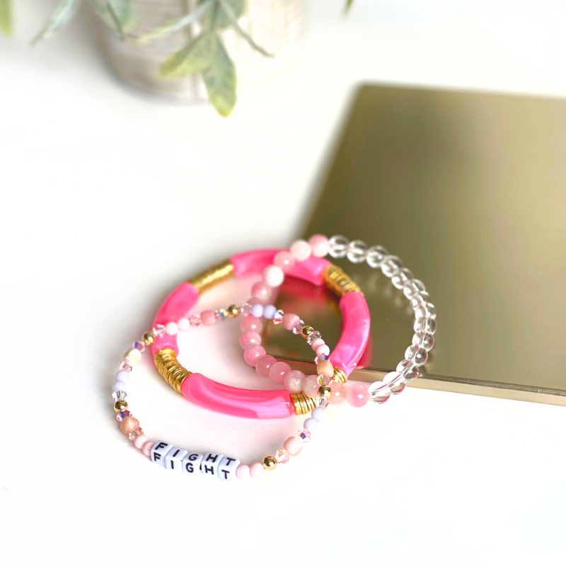 Pink beaded breast cancer awareness bracelet set. This very pink 3-piece bracelet set is curated with pink acrylic bangle, clear round quartz beads, pink beads and word beaded bracelet. Proceeds will be donated to the Susan G. Komen Foundation.