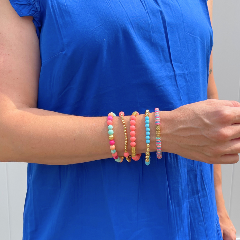 5-peice blue and peach matte acrylic beaded bracelet stack. This bracelet stack also includes a letter bead gold beaded bracelet and a gold beaded bracelet with mother of pearl heart charms.