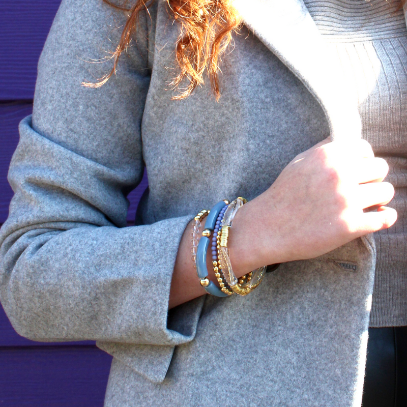 This 5-piece blue beaded stretch bracelet set is the perfect statement piece. With its simple colors, it is designed with 18K gold filled beads and natural Brazilian clear quartz beads, and blue glass beads. Blue and clear with gold acrylic bangles..