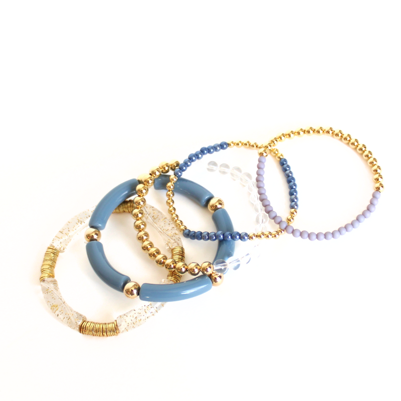 This 5-piece blue beaded stretch bracelet set is the perfect statement piece. With its simple colors, it is designed with 18K gold filled beads and natural Brazilian clear quartz beads, and blue glass beads. Blue and clear with gold acrylic bangles..