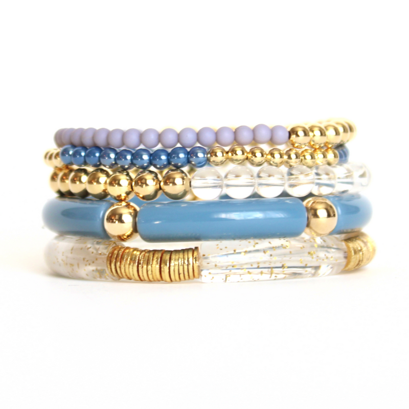 This 5-piece blue beaded stretch bracelet set is the perfect statement piece. With its simple colors, it is designed with 18K gold filled beads and natural Brazilian clear quartz beads, and blue glass beads. Blue and clear with gold acrylic bangles..