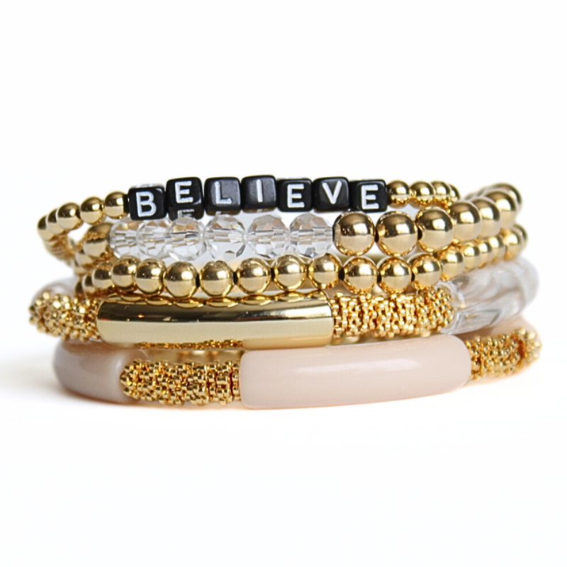 5-Piece 18K gold beaded stretch bracelet set with clear glass beads. Gold, clear and cream acrylic tube beads with gold accents. Black cubed acrylic letter beads that are personalizable.