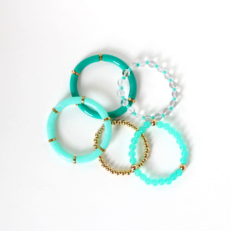 Bracelet stack with five bracelets. 2 bracelets are green bangles with gold plated flats. The third bracelet is an acrylic bracelet with gold filled beads. A clear quartz bracelet with green 4mm acrylic beads and a gold filled beaded bracelet complete the stack.