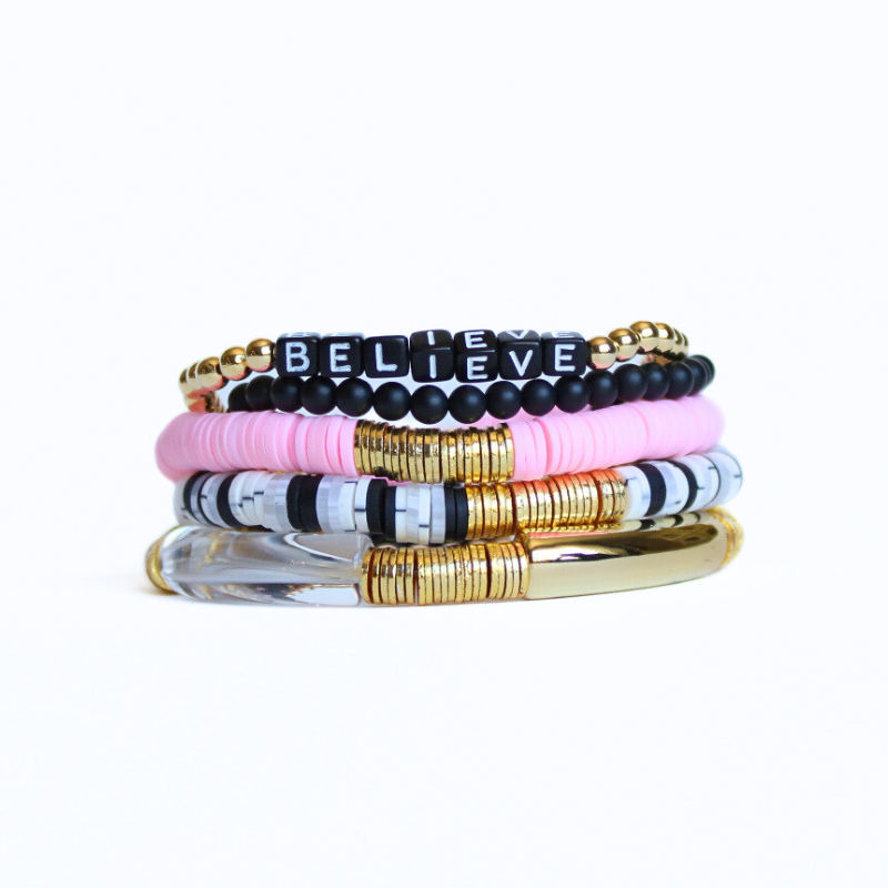This 5-piece pink and black beaded stretch bracelet set is the perfect statement piece. Designed with 18k gold filled beads, black glass beads and black acrylic cubed letter beads. The polymer clay beads add the perfect touch of pink. The gold and clear acrylic bangles add a modern touch.