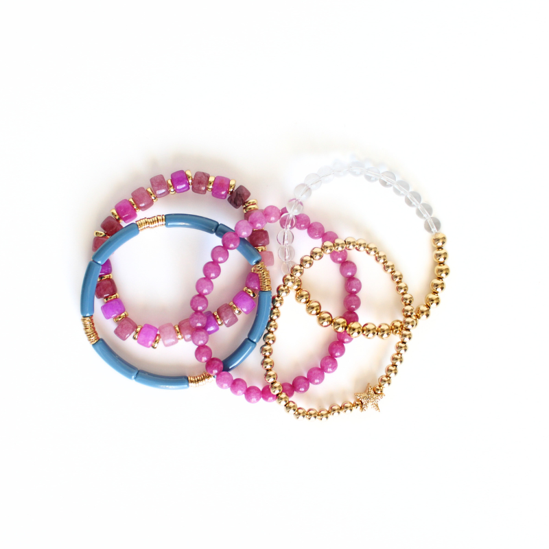 5-Piece purple beaded stretch bracelet set with 18k gold filled beads. The two gold beaded bracelets are designed with clear Brazilian quartz beads and a 14k gold forte charm. The two purple beaded bracelets are designed with forte gemstone beads and jade round beads. The skinny blue acrylic bangle adds the perfect touch.