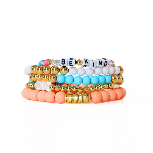5-piece stacking bracelet with peach and blue acrylic beads. White acrylic and white mother of pearl heart charms are accent with gold filled round beads. A dainty letter bead with rainbow seed beads complete the set.