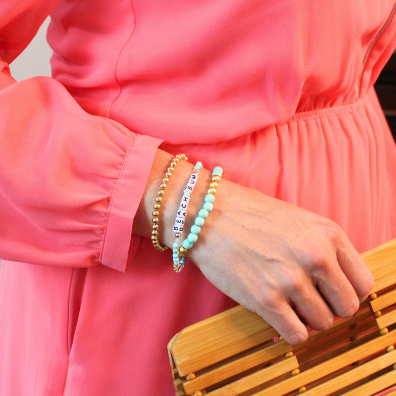 Model wearing three bracelets. First bracelet is a 4mm18k gold filled beaded bracelet, second is a blue jasper beaded stretch bracelet with personalized letter beads and the third a mint wooden stretch bracelet with brushed gold beads.