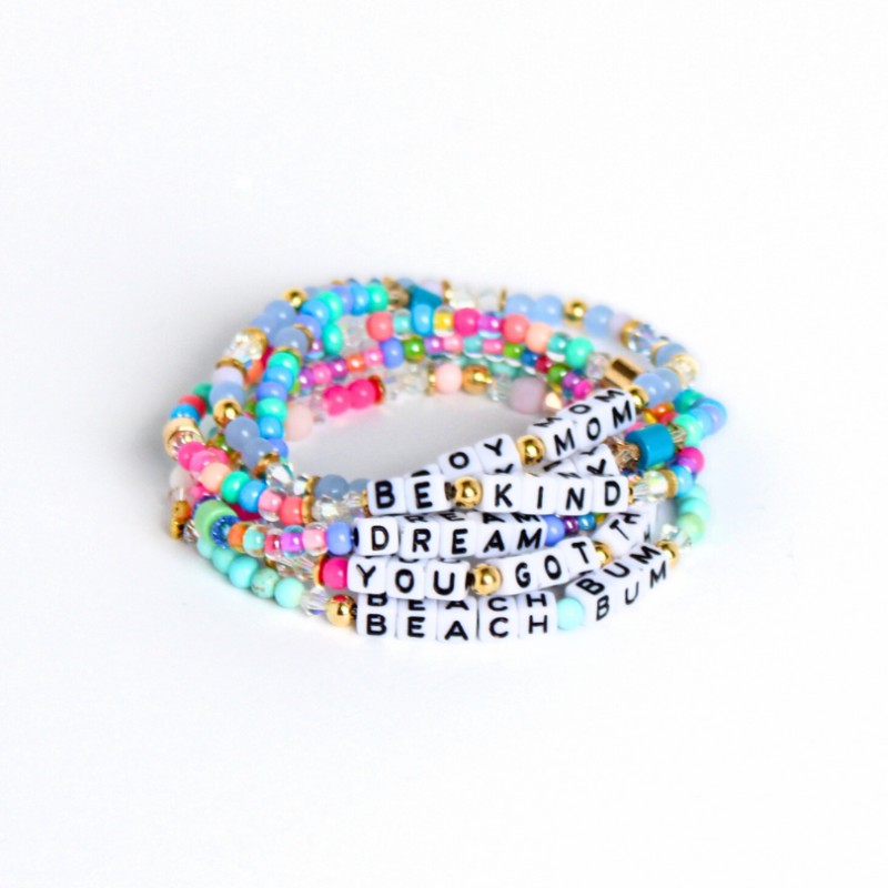 Stacks of different letter bead bracelet designs. Each bracelet is designed with 5mm white cubed letter beads with black letters. Bracelets are full of bold colors and can be personalized.