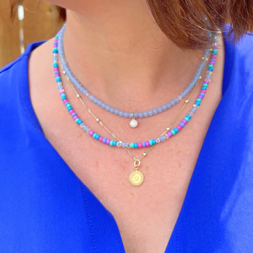 Model wearing 3 necklaces. The gold filled satellite necklace has a round gold plated coin charm. 2 other necklaces are dainty seed bead with blue, green and purple necklaces.