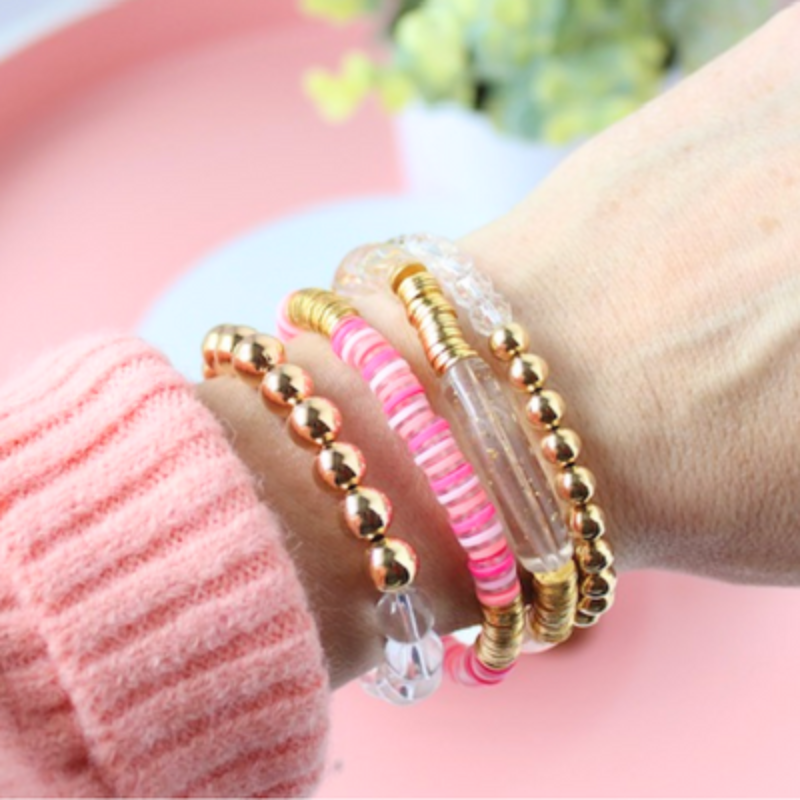 Model wearing a pink and gold bracelet stack. Designed with a pink stripe polymer clay beaded stretch bracelets and gold-filled beaded bracelets with acrylic tubes and clear quartz gemstones
