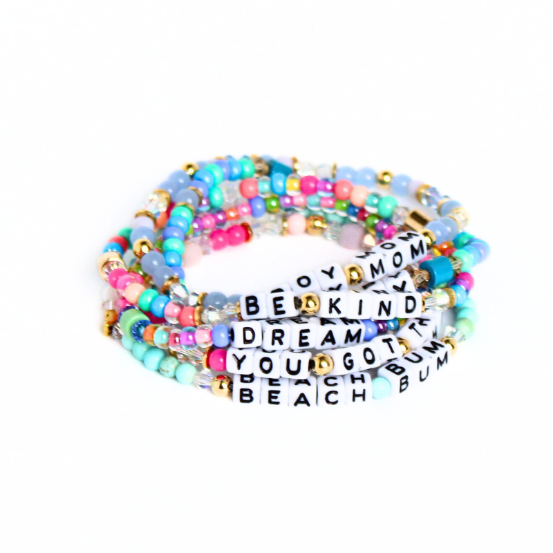 Stacks of different letter bead bracelet designs. Each bracelet is designed with 5mm white cubed letter beads with black letters. Bracelets are full of bold colors and can be personalized.