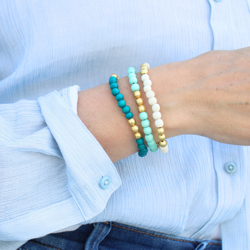 Model wearing 3-peice turquoise, mint and white lightweight wood stretch beaded bracelet set. All three bracelets accented with brushed gold beads.