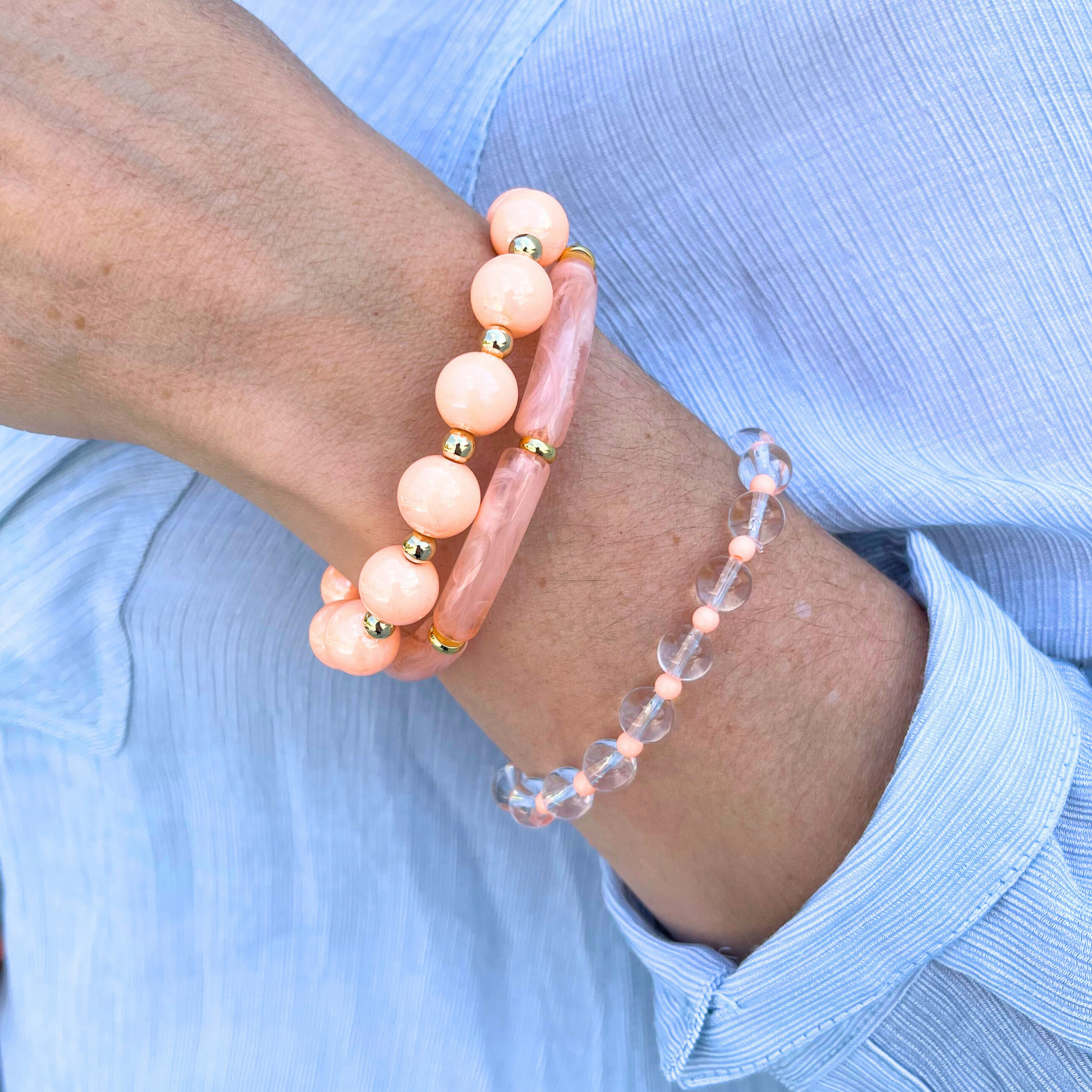 Model wearing a 3-peice peach golden hour beach bracelet set. Designed with 8mm skinny acrylic bamboo tubes with alternating gold flats. Chunky 12mm peach iridedescent acrylic beads with alternating 5mm gold beads. 6mm clear quartz round beads with alternating 4mm peach acrylic beads.