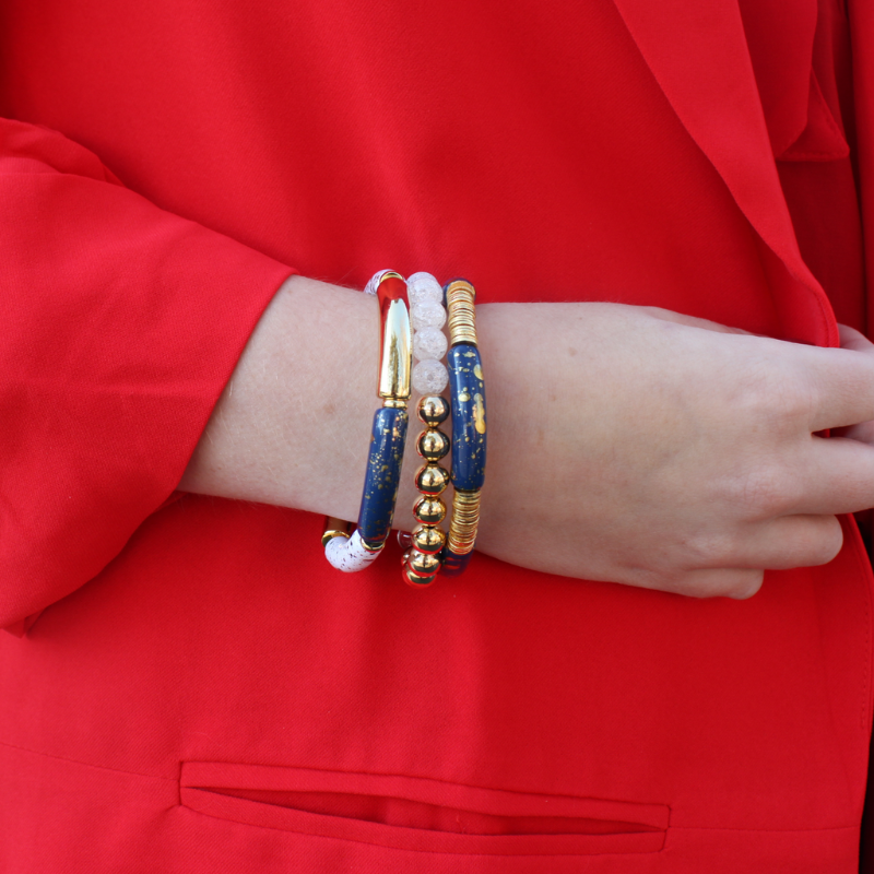 Model is wearing a three piece, dark blue beaded bracelet stack with a red blazer