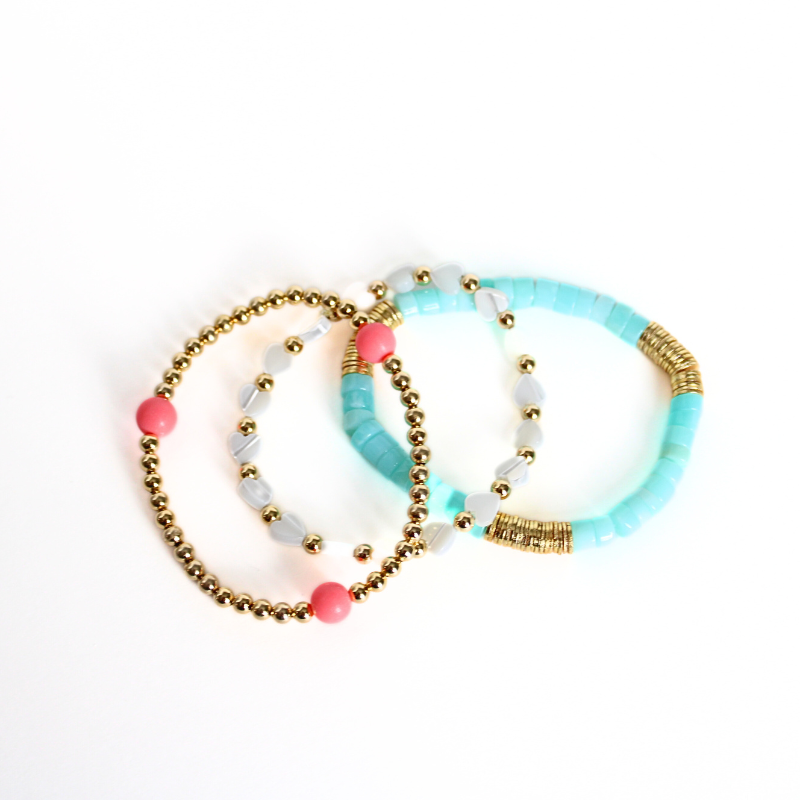 3-piece bracelet stack designed with a dainty gold beaded bracelet, blue opal heishi beaded bracelet with gold flat beads and a dainty mother of pearl heart shape beaded bracelet