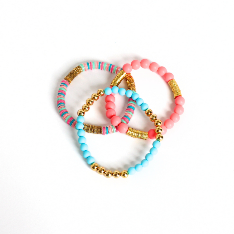 Bracelet stack with 3 beaded stretch bracelets. The Key West bracelet set is designed with blue and watermelon acrylic beads. A polymer clay beaded bracelet has pink, blue and peach rainbow design with flower gold plated flats. 18k gold fillec round beads adds long lasting sparkle.