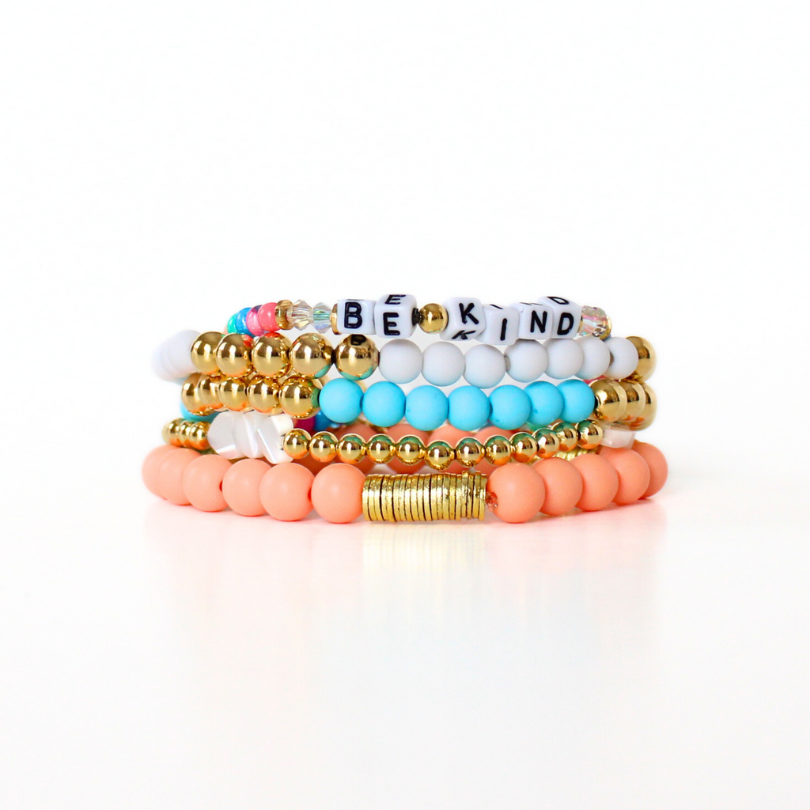 5-peice blue and peach matte acrylic beaded bracelet stack.  This bracelet stack also includes a letter bead gold beaded bracelet and a gold beaded bracelet with mother of pearl heart charms.