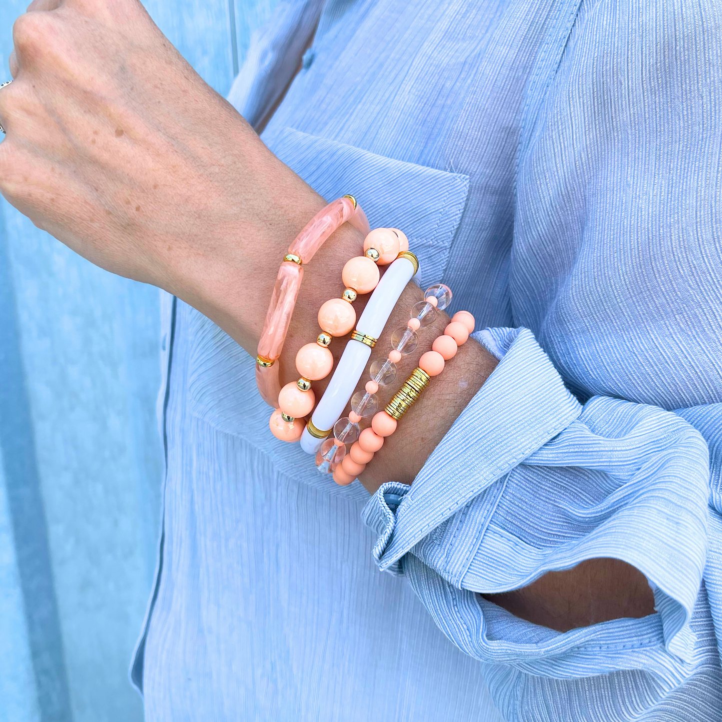 Model wearing 5-peice peach golden hour bracelet stack. This bracelet stack has two 8mm skinny bamboo acrylic tube bangles; peach marble and white. Clear 6mm quartz round beads with alternating 4mm peach acrylic beads. 12mm chunky acrylic round beads with alternating gold filled round beads. And also designed with 6mm peach acrylic round beads with gold plated flats.