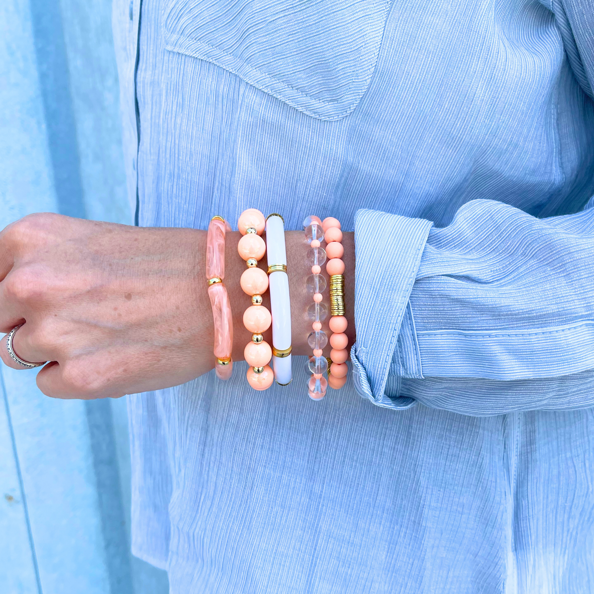 Model wearing 5-peice peach golden hour bracelet stack. This bracelet stack has two 8mm skinny bamboo acrylic tube bangles; peach marble and white. Clear 6mm quartz round beads with alternating 4mm peach acrylic beads. 12mm chunky acrylic round beads with alternating gold filled round beads. And also designed with 6mm peach acrylic round beads with gold plated flats.