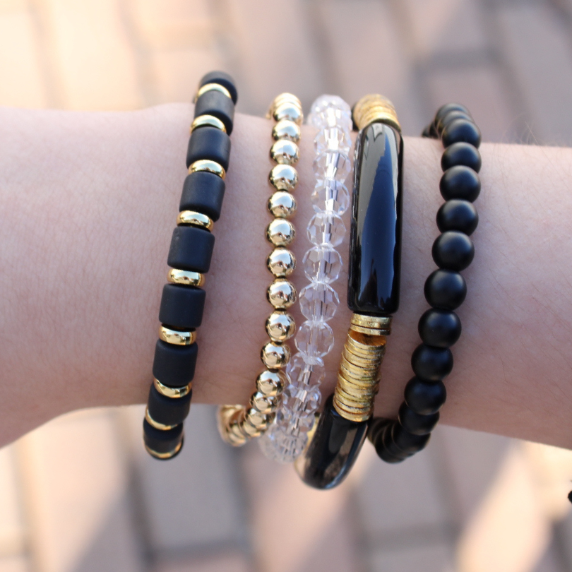 Model wearing a 5-peice bracelet stack desinged with black polymer, acrylic and gold-filled beads.
