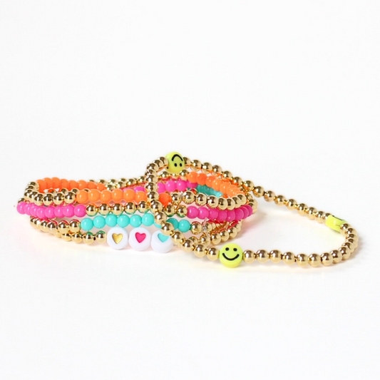 This dainty 5-piece stretch bracelet stack is designed with 4mm 18k gold filled round beads. 3 bracelets are adorned with 4mm acrylic beads: orange, pink and blue. White acrylic beads with colored heart centers accent one bracelet. And the last bracelet has a playful yellow smiley face acrylic bead