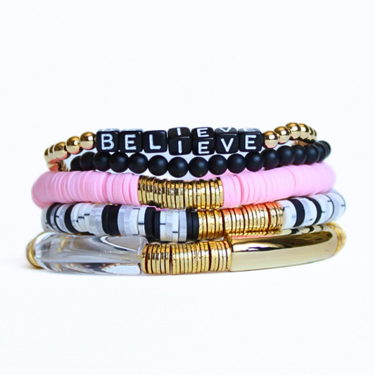 This 5-piece pink and black beaded stretch bracelet set is the perfect statement piece. Designed with 18k gold filled beads, black glass beads and black acrylic cubed letter beads. The polymer clay beads add the perfect touch of pink. The gold and clear acrylic bangles add a modern touch.