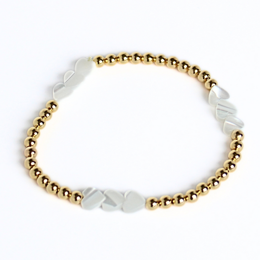 Dainty 4mm 18k gold filled round beaded stretch bracelet accented with mother of pearl heart charms.
