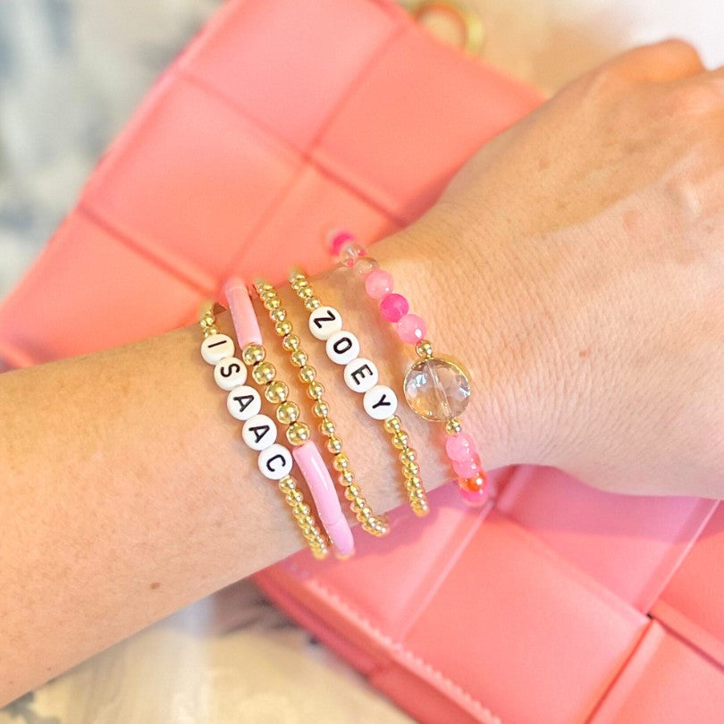 5-piece pink and gold beaded bracelet set.  This fun set is designed with two gold beaded bracelets with custom letter bead bracelets, a skinny pink acrylic beaded bangle and a pink faceted gemstone bracelet with a crystal charm.