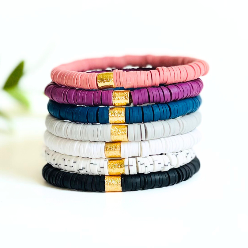 Stack of polymer clay beaded heishi bead bracelets with gold plated cylinder charm